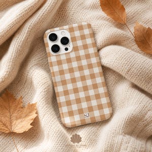 May include: A smartphone case featuring a tan and white gingham check pattern. The case has a cutout for a triple-lens camera system on the top left corner. The letters SJ are printed in a small, dark serif font near the bottom right corner.