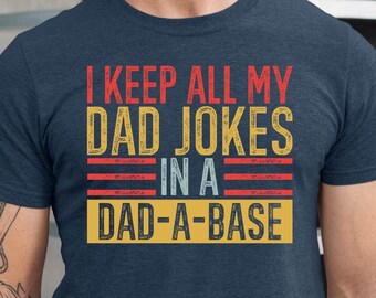 May include: A navy blue t-shirt with a vintage-style graphic that reads "I keep all my dad jokes in a dad-a-base".