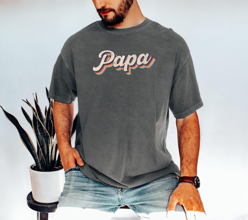 May include: A dark gray t-shirt with a retro-style graphic that says "Papa" in colorful letters.