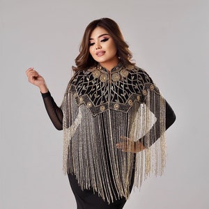 Puede incluir: Un chal negro y dorado con flecos de cuentas. El chal tiene un cuello alto y está decorado con bordados florales.