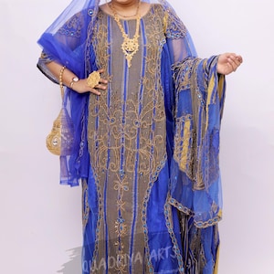 Peut inclure: Une robe brodée bleue et dorée avec une superposition transparente. La robe a un col haut et des manches longues. La femme porte un collier et des boucles d'oreilles en or.