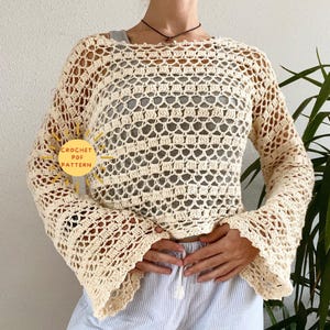 May include: A crochet top with long bell sleeves. The top is made with a delicate open stitch pattern and is a light cream color. The text "CROCHET PDF PATTERN" is visible in the image.
