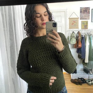May include: A dark green crocheted sweater with long sleeves and a round neckline.
