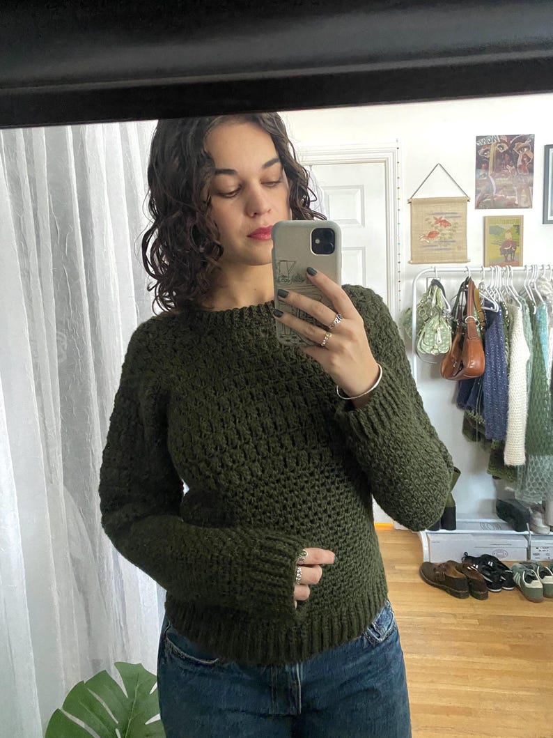 May include: A dark green crocheted sweater with long sleeves and a round neckline.