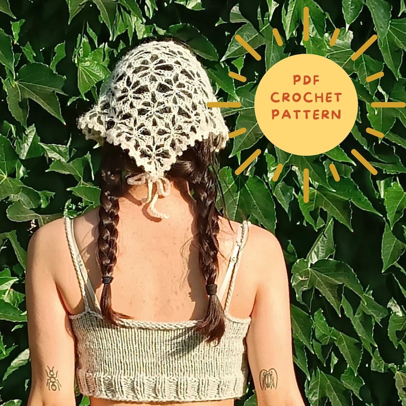 May include: A white crochet sun hat with a delicate floral pattern. The hat is worn by a person with long brown hair styled in braids. The image includes the text "PDF CROCHET PATTERN".
