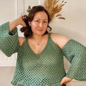 May include: A green crochet top with a v-neck and open shoulders. The top has a crocheted lace trim around the bottom.