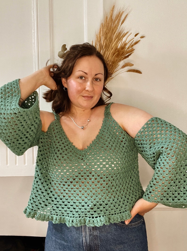 May include: A green crochet top with a v-neck and open shoulders. The top has a crocheted lace trim around the bottom.