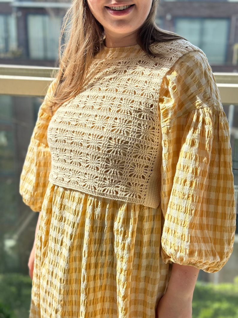 K&ouml;nnte beinhalten: Ein gelbes und wei&szlig;es Gingham-Kleid mit einem geh&auml;kelten Oberteil. Das Kleid hat einen runden Ausschnitt und Puff&auml;rmel.