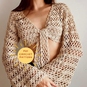 Op de afbeelding: Een gehaakt topje met een strik aan de voorkant en lange mouwen. Het topje is beige van kleur en heeft een delicaat opengewerkt patroon. De tekst "PDF CROCHET PATTERN" is zichtbaar in de afbeelding.