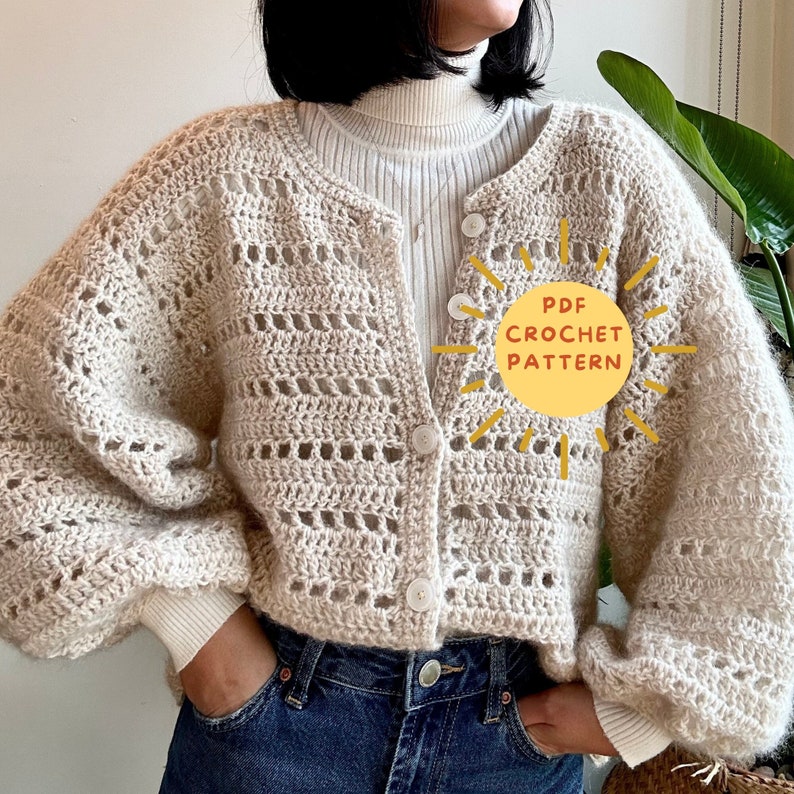 Op de afbeelding: Een cr&egrave;mekleurig, open geweven gehaakt vest met grote, ronde knopen. Het vest heeft een ronde halslijn en lange, pofmouwen. De tekst "PDF CROCHET PATTERN" wordt op de afbeelding weergegeven.