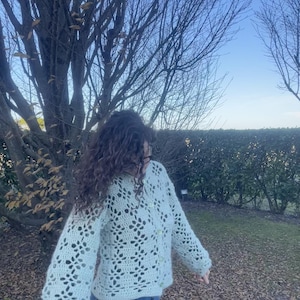 Pu&ograve; includere: Un cardigan di uncinetto verde chiaro con chiusura a bottoni e un motivo a pizzo. Il cardigan ha maniche lunghe e una vestibilit&agrave; rilassata.