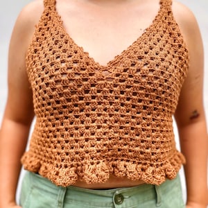 Op de afbeelding: Een bruin gehaakt tanktop met een gerimpelde zoom. Het topje is gemaakt met een delicaat open steekpatroon.