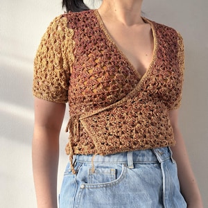 K&ouml;nnte beinhalten: Geh&auml;keltes Wickel-Top in Braun- und Goldt&ouml;nen. Das kurz&auml;rmelige Oberteil hat einen V-Ausschnitt und ein Wickeldesign mit Bindeb&auml;ndern an der Taille. Die offene Webart des H&auml;kels erzeugt einen strukturierten Look.