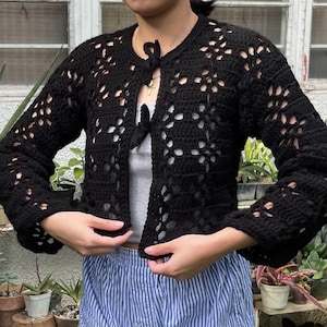 Pu&ograve; includere: Un cardigan in crochet nero con un nodo sul collo. Il cardigan ha una vestibilit&agrave; ampia e una lunghezza corta. &Egrave; realizzato con un delicato motivo a punto aperto.