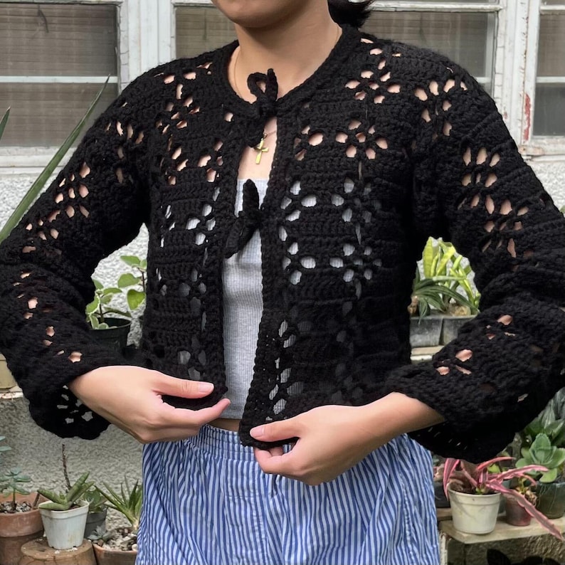 Pu&ograve; includere: Un cardigan in crochet nero con un nodo sul collo. Il cardigan ha una vestibilit&agrave; ampia e una lunghezza corta. &Egrave; realizzato con un delicato motivo a punto aperto.