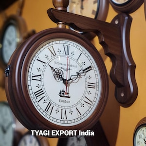 May include: A double-sided, wooden wall clock with a cream-colored face and black Roman numerals. The clock features the text "Jeffersonn & Smith London" and is mounted on a dark brown wooden bracket. The clock is surrounded by other clocks.