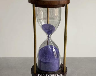 May include: An hourglass with a wooden frame and brass supports. The clear glass bulb contains purple sand. The hourglass is a decorative item, and the base has the text "TYAGI EXPORT India".