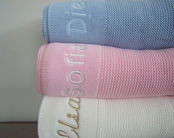 May include: Three knitted baby blankets stacked on top of each other. The top blanket is light blue with the name "Riley" embroidered in white. The middle blanket is pink with the name "Sofia" embroidered in white. The bottom blanket is white with the name "Eliza" embroidered in gold.