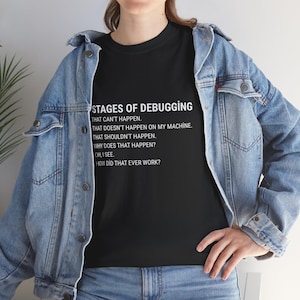 Może przedstawiać: Czarny t-shirt z napisem "STAGES OF DEBUGGING" i listą etapów debugowania w białej czcionce. Koszulka jest noszona z niebieską kurtką dżinsową.