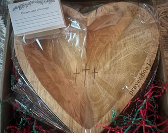 May include: A heart-shaped wooden prayer bowl with three engraved crosses, packaged in a cardboard box with red and green paper filler. A small card with the text "Prayers and Blessings" is included.