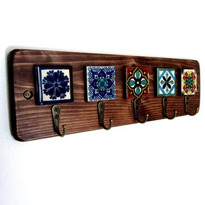 May include: A wooden key holder with five decorative ceramic tiles and bronze hooks. The tiles feature colourful floral patterns in blue, green, red, and yellow. The wood is stained a dark brown colour.