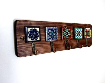 May include: A wooden key holder with five decorative ceramic tiles and bronze hooks. The tiles feature colorful floral patterns in blue, green, red, and yellow. The wood is stained a dark brown color.