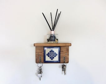 May include: A rustic wooden wall shelf with a decorative blue and white tile insert. The shelf holds a glass diffuser bottle with black reeds and a set of keys hanging below. The shelf is 12 inches wide.