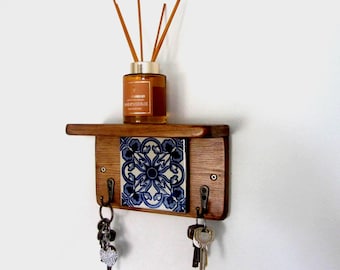 May include: A wooden key holder with a shelf, a decorative blue and white tile, and three metal hooks. A bottle of fragrance diffuser with reeds sits on the shelf. Keys hang from the hooks, creating a functional and decorative wall accent.