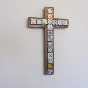 May include: Wooden cross with decorative tiles. The cross is made of dark wood and features colorful square tiles with various patterns. The tiles are arranged in a grid pattern, adding visual interest to the religious symbol.