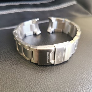 May include: A silver watch band with a clasp that reads "30 bar/3 ATM".
