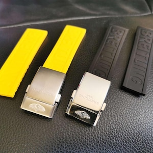 Puede incluir: Tres correas de reloj, dos amarillas y una negra, con hebillas metálicas que dicen "Breitling".