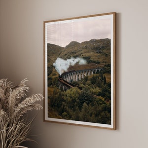 Può includere: Un treno a vapore nero viaggia attraverso una valle verde lussureggiante, attraversando un ponte ad arco in pietra. Il treno emette fumo e vapore, creando una scena drammatica.