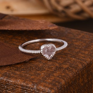 Könnte beinhalten: Ein silberner Ring mit einem herzförmigen Rosenquarz-Edelstein. Der Ring hat eine strukturierte Band.