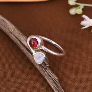 May include: A silver ring with a red gemstone and a white gemstone. The ring is designed with a twisted band.