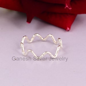 Op de afbeelding: Een zilveren ring met een golvend, getextureerd ontwerp. De ring is simpel en elegant.