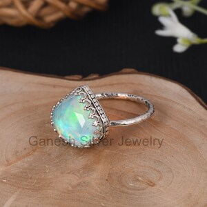 May include: A silver ring with a teardrop-shaped opal gemstone set in a detailed silver bezel. The ring band is textured and has a hammered finish.