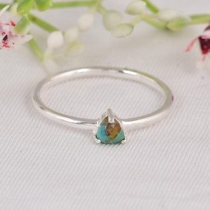 May include: A silver ring with a triangular turquoise stone. The ring has a thin band and a simple, elegant design. The turquoise stone has a mix of blue and brown colors.