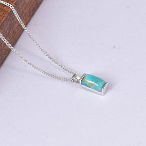 May include: A silver necklace featuring a rectangular turquoise pendant. The pendant is a vibrant blue-green color with brown veining. The chain is a delicate silver curb chain, and the pendant is set in a silver bezel.
