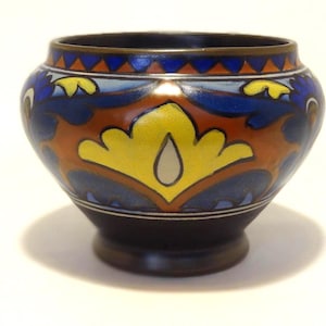 May include: A small, round, decorative ceramic vase with a dark brown base and rim. The vase features a colourful floral design in blue, orange, and yellow. The top rim has a gold band.
