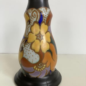 Könnte beinhalten: Eine dekorative Keramikvase mit schwarzem Boden und Deckel. Die Vase hat ein Blumendesign in Gelb-, Orange-, Lila- und Blautönen auf hellblauem und braunem Hintergrund. Die Vase hat eine bauchige Form.