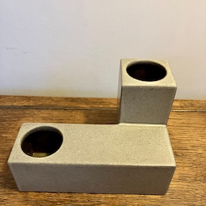 May include: A gray ceramic vase with two openings, shaped like the letter L. The vase has a speckled texture.
