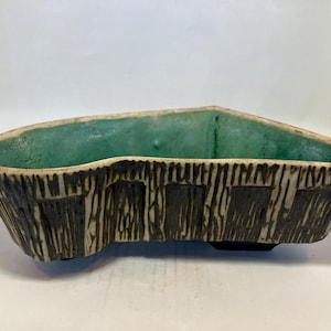 Op de afbeelding: Een keramische plantenbak met een getextureerde, schorsachtige buitenkant in bruin- en crèmetinten. De binnenkant is een levendige turquoise kleur. De plantenbak heeft een unieke, asymmetrische vorm, ideaal voor planten.