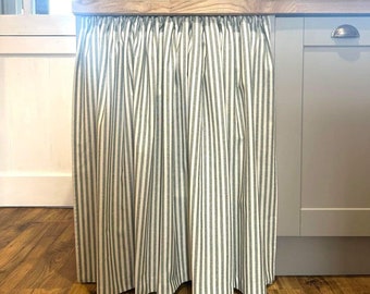 May include: A white kitchen island with a green and white striped fabric skirt. The island has a wooden countertop and a white cabinet.