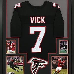 May include: A framed black Atlanta Falcons jersey with the number 7 and the name "VICK" on the back. The jersey is signed by Michael Vick. The frame includes four smaller photos of Vick in action.