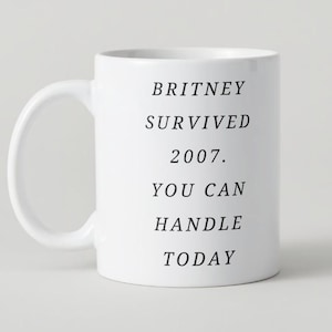 Puede incluir: Taza de cerámica blanca con texto negro que dice "Britney sobrevivió a 2007. Puedes manejar hoy."