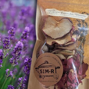 Peut inclure: Un sachet de mélange pour pot-pourri "Lavender Dreams" avec des tranches de pommes séchées, des pétales de rose et des boutons de lavande. L'emballage porte l'étiquette "SIM-R Handcrafted simmer Pot Mix". En arrière-plan, un champ de lavande violette.