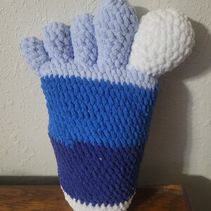 May include: A crocheted foot-shaped plush toy with blue, white, and light blue stripes. The toes are light blue and the heel is white.