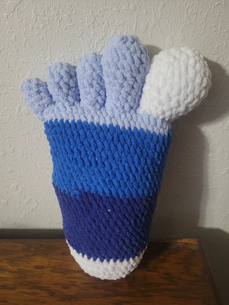 May include: A crocheted foot-shaped plush toy with blue, white, and light blue stripes. The toes are light blue and the heel is white.