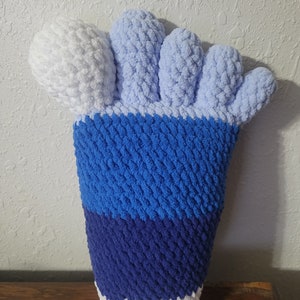 May include: A blue, white, and light blue crocheted foot-shaped pillow. The toes are white and light blue, the foot is blue, and the ankle is white and dark blue.