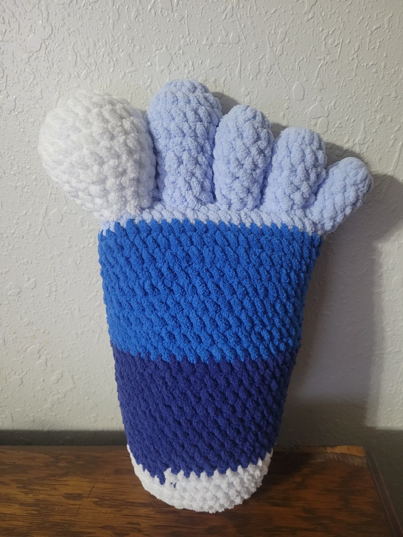 May include: A blue, white, and light blue crocheted foot-shaped pillow. The toes are white and light blue, the foot is blue, and the ankle is white and dark blue.